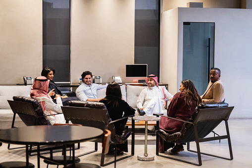Wide angle view of Saudi men and women in western and traditional attire sitting together, talking, and laughing.