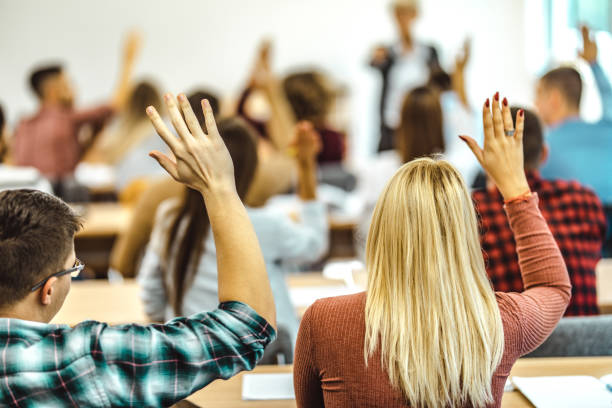 istock Back view of college students raising their arms on a class at lecture hall. 1396209257