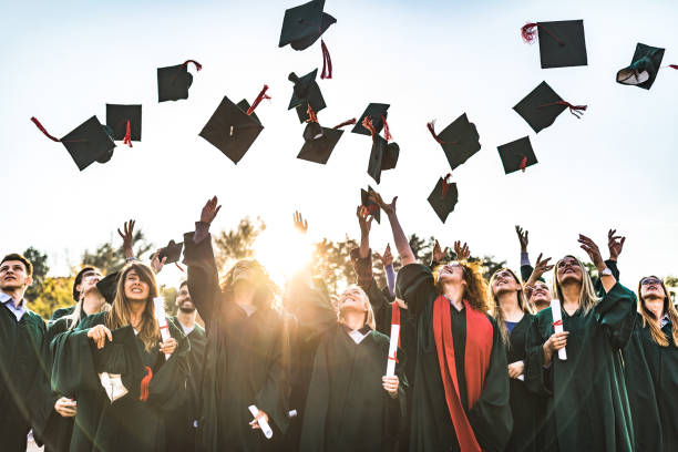 Graduation day! Large group of happy college students celebrating their graduation day outdoors while throwing their caps up in the air. graduation throwing cap stock pictures, royalty-free photos & images