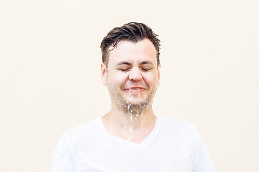 Wet young caucasian man in white t shirt with closed eyes and water is flowing from his face. Portrait, stress shock concept, lifestyle