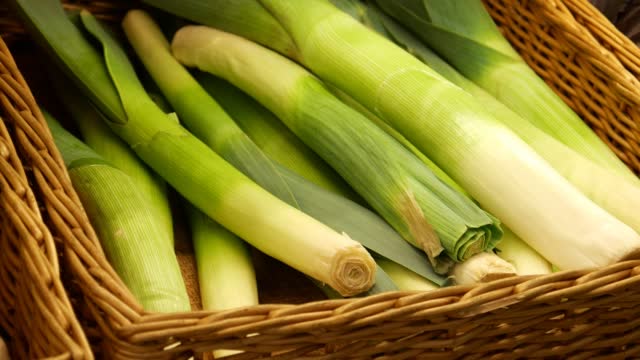 Close-up of many beautiful leeks in a wicker basket and a male hand takes one