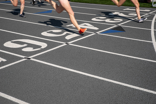 Outdoor track and fiield running race on a gray track with  numbered lanes and a finish line with copy space. Two runners cross the line.