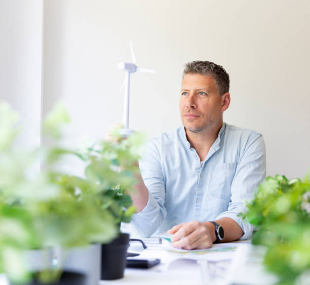 istock Business portrait of environmental engineer sitting at his work table and holding a model of a wind turbine in his hands 1396214972