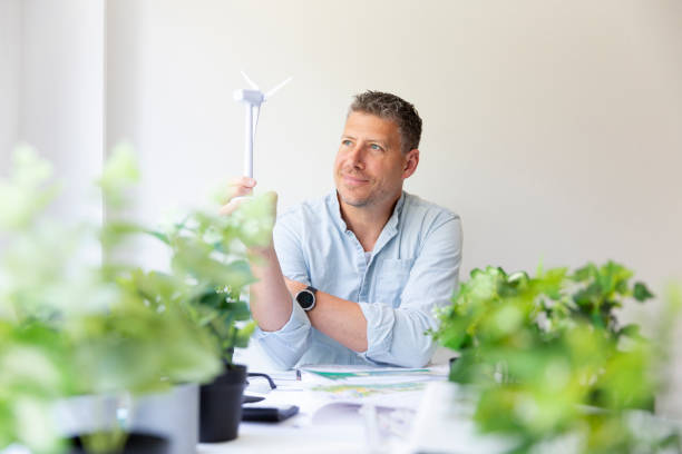 istock Business portrait of environmental engineer sitting at his work table and holding a model of a wind turbine in his hands 1396214980