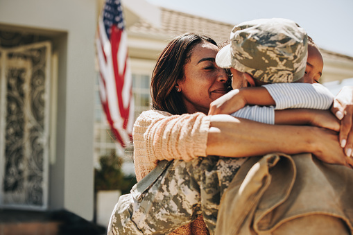 American serviceman saying his goodbyes to his family at home. Brave soldier embracing his wife and daughter before leaving for war. Patriotic man leaving to go serve his country in the military.