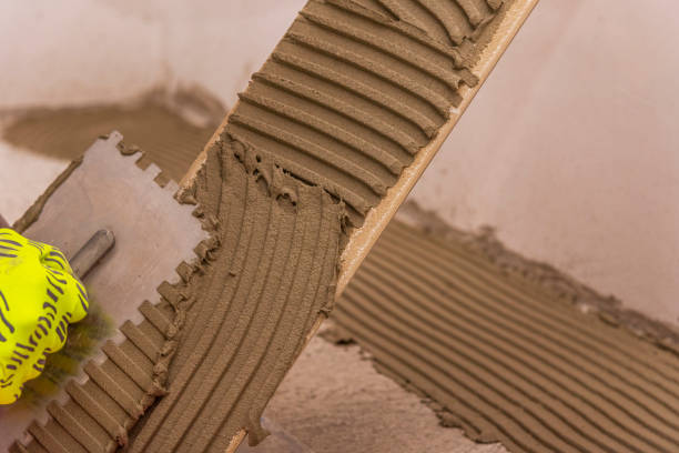 istock Worker placing ceramic floor tiles on adhesive surface, leveling with rubber hammer. 1396216533