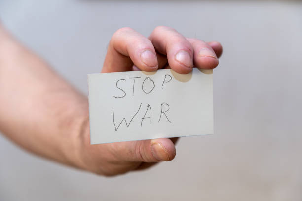 istock Stop War. Words written in jagged letters. A man's hand holds a white paper rectangle with text against a gray background. 1396216939