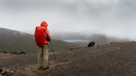 Hiking Tama Lakes track. Man looking at lower Tama lake in the mist. Tongariro National Park.