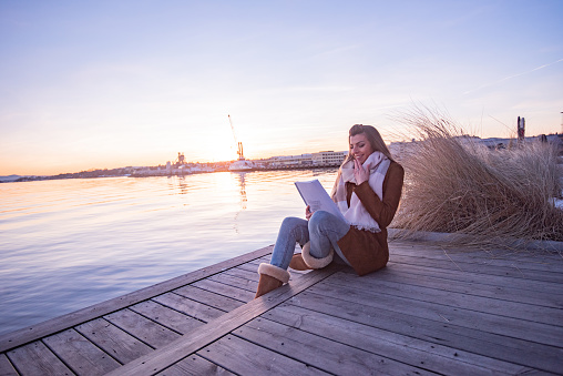 Young female student reading a book and sitting on the pier