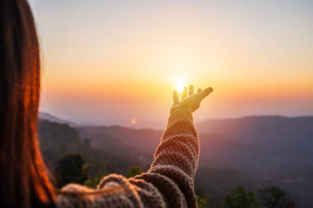 Young woman hand reaching for the mountains during sunset and beautiful landscape stock photo