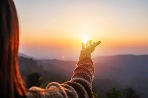 Photo of Young woman hand reaching for the mountains during sunset and beautiful landscape