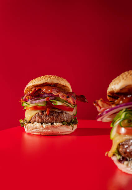 istock Bold fresh cheeseburger loaded with lettuce, cucumber, tomato and bacon on vibrant red 1396221407