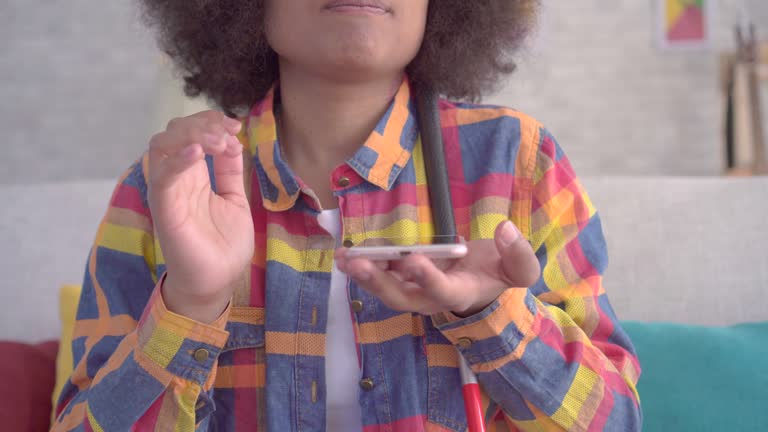 blind african woman with an afro hairstyle uses voice assistant on your smartphone sitting on the couch close up