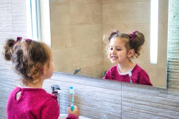 istock Young cute female kid looking at her reflection in the bathroom mirror while brushing her teeth 1396228546