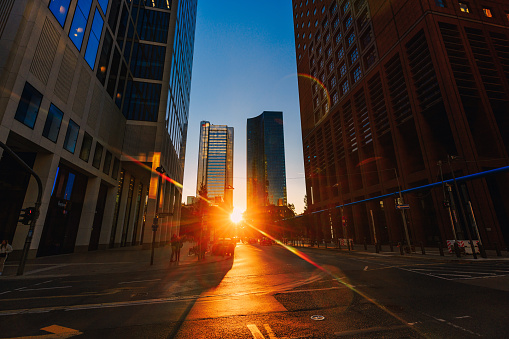 Sun setting with lens flare between business skyscrapers in Frankfurt am Main, clear sky and empty street without traffic