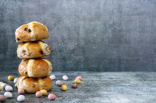 Stock photo showing close-up view of stack display of freshly baked, homemade Easter hot cross buns, home baking concept. These traditional spiced sweet buns are made and sold over the Easter period, with the cross symbol on the glazed top being made from a flour and water paste, and symbolising Christianity.