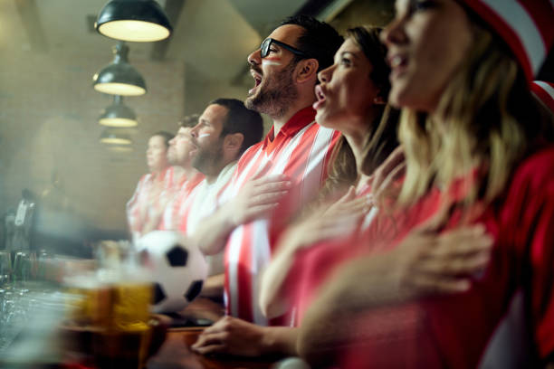 Soccer fans singing the anthem before the game in a bar. Group of sports fans singing the national anthem while watching the match on TV in a bar. Focus is on man with eyeglasses. national anthem stock pictures, royalty-free photos & images