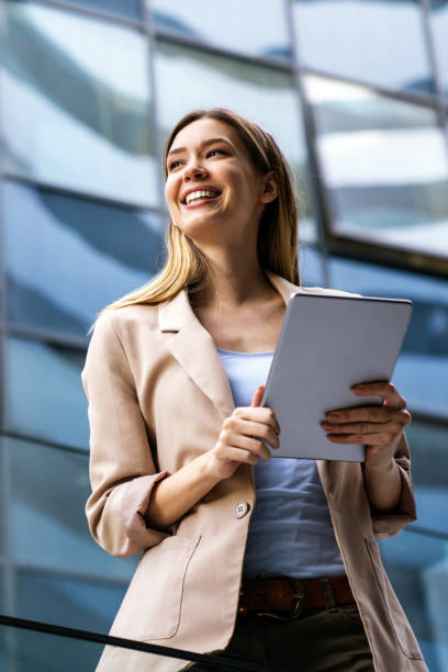 istock Successful businesswoman using a digital tablet while standing in front of business building. 1396234375