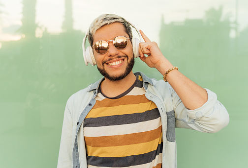 Young latin man with glasses listening to happy music looks at camera.