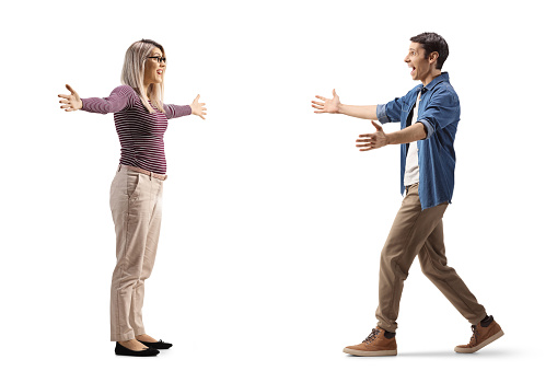 Full length profile shot of a young man and woman meeting each other with open arms isolated on white background