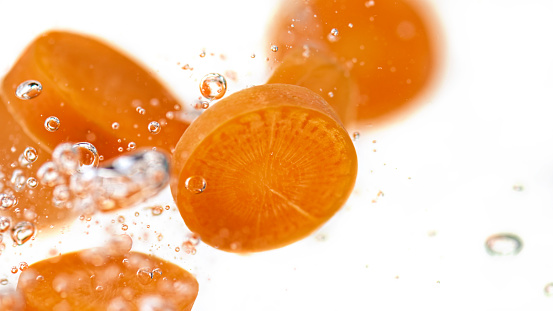 Close-up of carrot slices in water against white background.