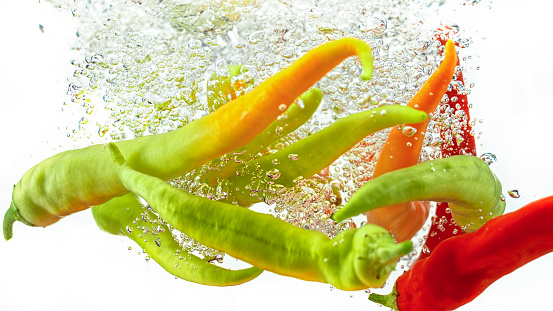 Close-up of chilli peppers in water against white background.