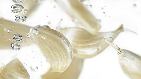 Close-up of garlic cloves in water against white background.