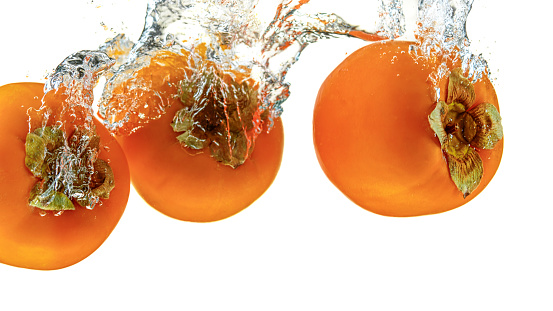 Close-up of persimmons in water against white background.
