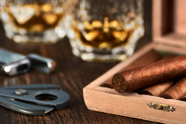 vue d’une boîte en bois avec des cigares cubains, un briquet et un cutter. nature morte avec deux verres de whisky sur la table. - cigar whisky bar cognac photos et images de collection