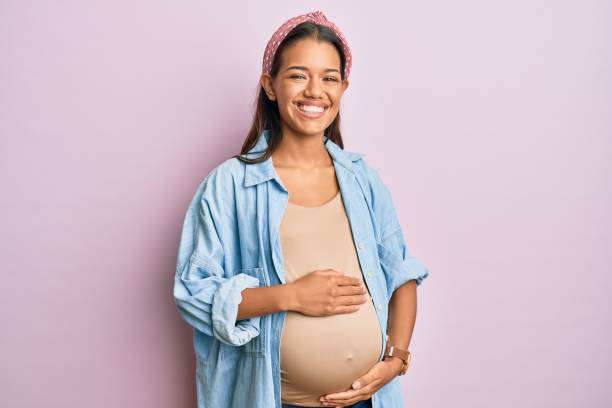 Beautiful hispanic woman expecting a baby, touching pregnant belly smiling and laughing hard out loud because funny crazy joke. stock photo