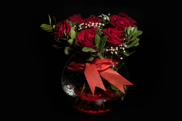 istock Red roses in glass vase isolated on black background. 1396247286