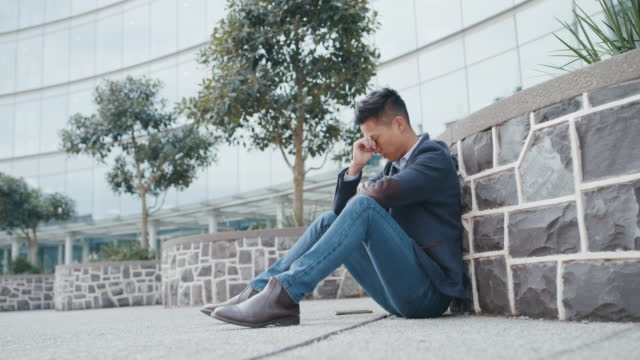 A business man sitting in the street in the city and looking stressed. A young businessman looking unhappy after receiving bad news against an urban background