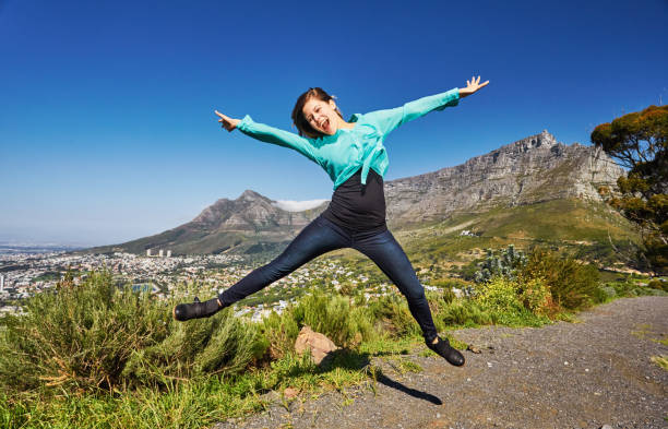 beautiful young woman tourist jumps for joy in front of table mountain, cape town, south africa - arms outstretched teenage girls jumping flying imagens e fotografias de stock