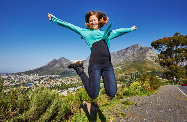 красивая молодая туристка прыгает от радости перед столовой горой, кейптаун, южная африка - arms outstretched teenage girls jumping flying стоковые фото и изображения