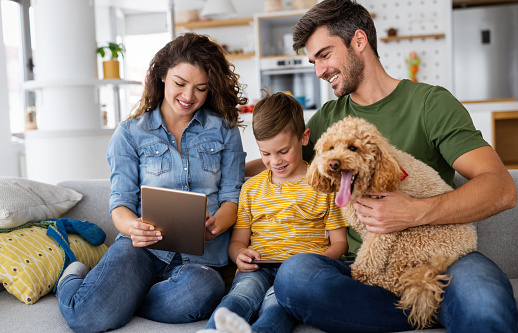 Happy young family with modern devices and dog having fun, playing at home
