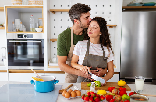 Young happy couple is enjoying and preparing healthy meal in their kitchen at home