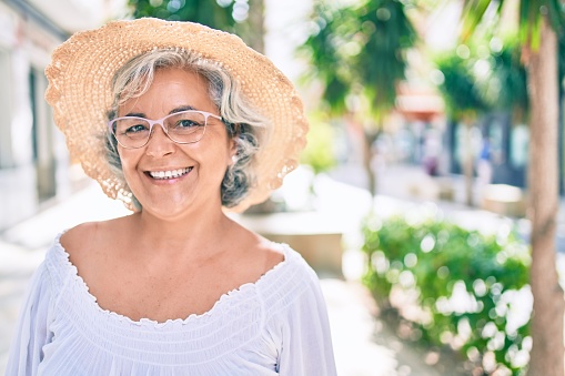 Middle age woman with grey hair smiling happy wearing summer hat outdoors
