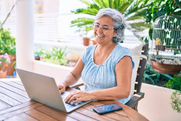 Middle age woman with grey hair smiling happy relaxing sitting at the terrace working from home stock photo