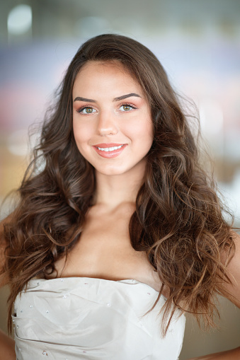 Beautiful young fashion model with long brown hair wearing gray colored strapless top, standing outdoors and posing, looking at camera and smiling