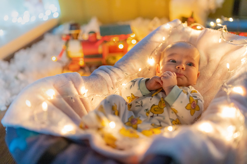 Baby girl lying on blanket against Christmas lights at home