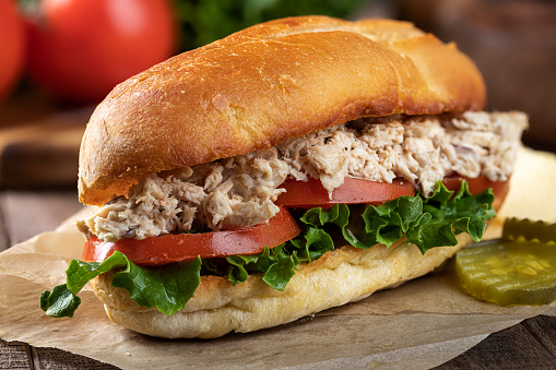 Closeup of a tuna salad, lettuce and tomato submarine sandwich with pickles