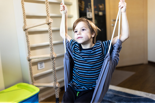 Little boy sitting on a swing in his bedroom and looking away