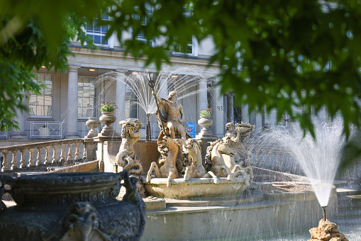 Neptunes fountain in the centre of Cheltenham in full flow on a sunny spring day. It depicts the Greek god Neptune in a shell-chariot, being drawn by four sea-horses and heralded by conch-shell blowing merman