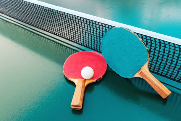 Table tennis rackets and ping-pong balls on green table surface with net stock photo