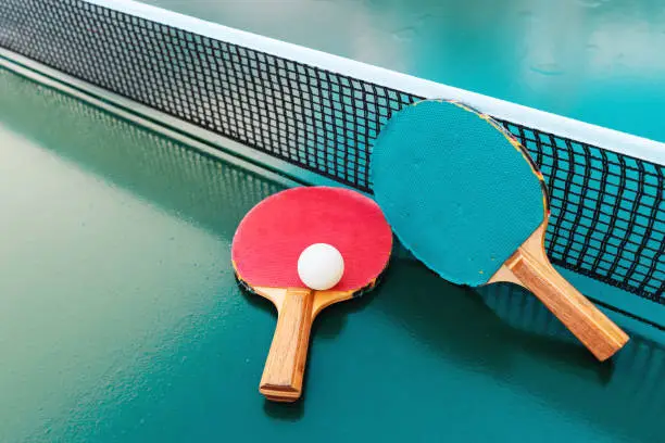 Table tennis rackets and ping-pong balls on green table surface with net, selective focus