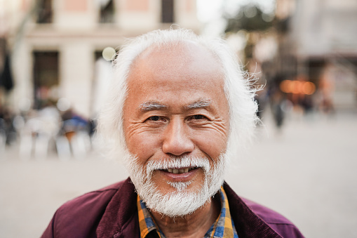 Asian senior man smiling on camera outdoor - Focus on face