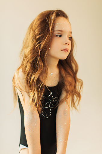 Little cute girl with long blonde curly hair in studio on white background. Beauty makeup with glitter. Childhood. Stylish child. Princess. Beautiful face. Lips gloss