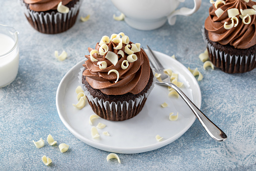 Dark chocolate cupcakes topped with whipped ganache frosting and white chocolate curls served with coffee