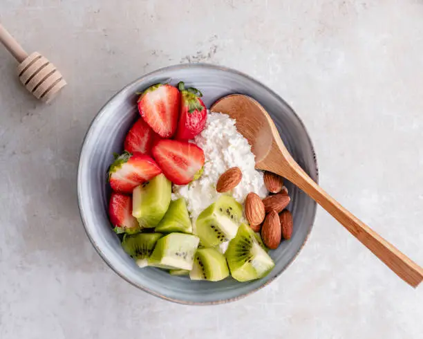 Top down view of a ceramic bowl with cottage cheese, strawberries, kiwi and almonds.