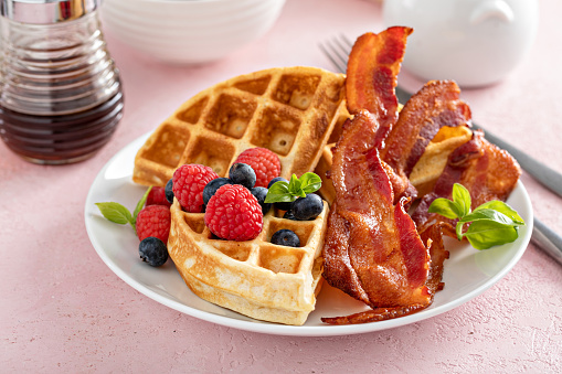 Belgian waffles with crispy bacon and fresh berries for breakfast, served with maple syrup